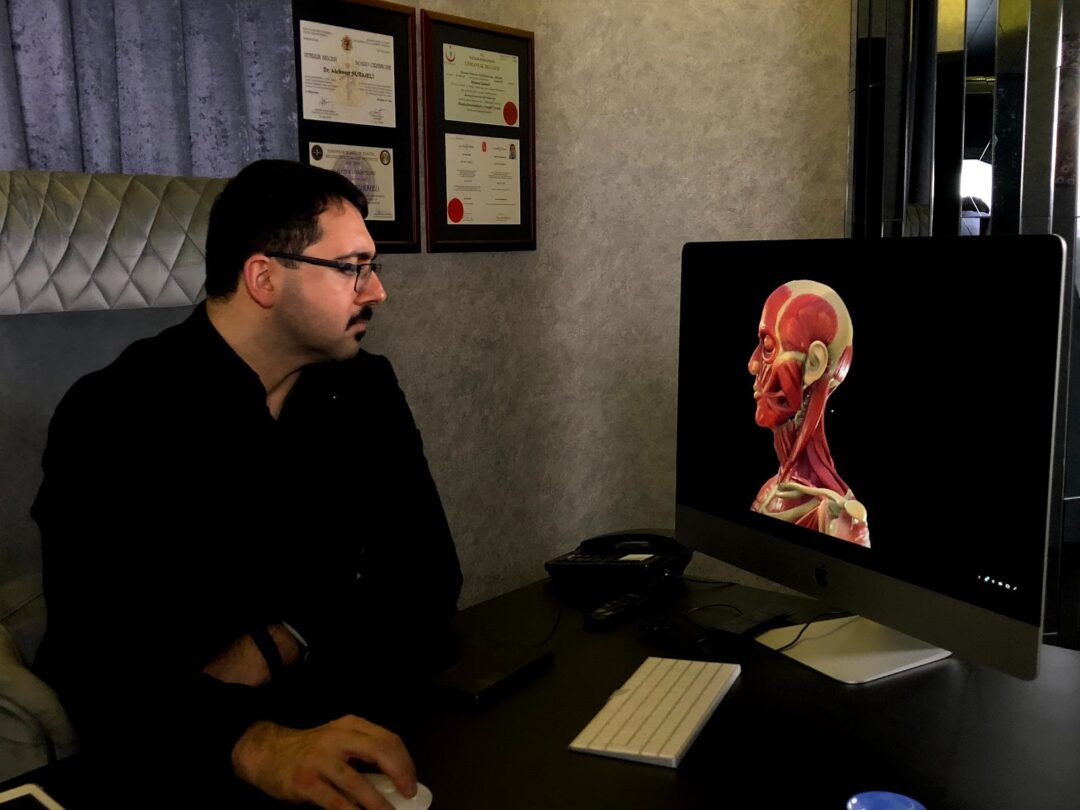 Dr. Mehmet Sürmeli studying facial anatomy during surgical planning, board certificates on the wall